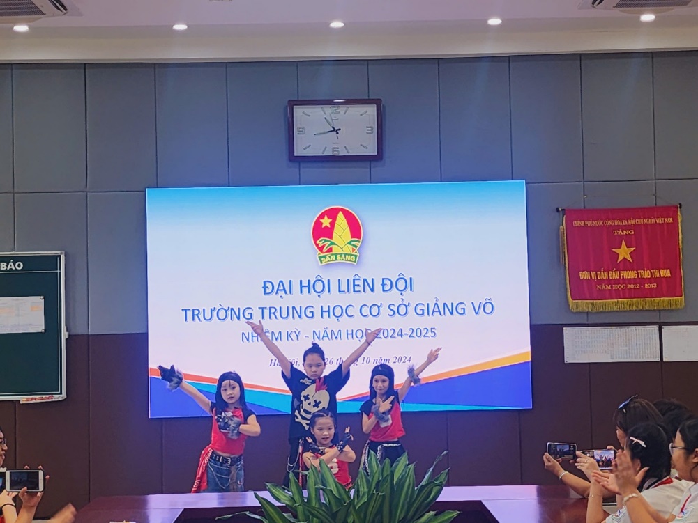 A group of kids standing in front of a large screenDescription automatically generated